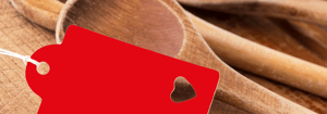 Rote Anhängerkarte mit Herz-Ausstanzung vor einem Hintergrund aus hölzernen Kochlöffeln – Symbol für einfache und schnelle Kochrezepte.