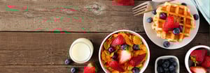 Frisches und gesundes Frühstück mit Cornflakes, frischen Erdbeeren, Blaubeeren, Waffeln und einem Glas Milch auf rustikalem Holztisch – Symbol für Energie und bewusste Ernährung im Rahmen der DATAGROUP Gesundheitswoche.