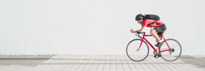 Sportlicher Radfahrer in roter Kleidung und Helm fährt auf einem Rennrad vor einer hellen Wand – Symbolbild für die Aktion Stadtradeln bei DATAGROUP.