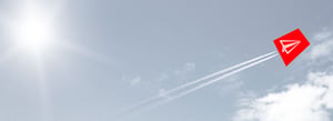 Ein Papierflieger im roten Trapez startet durch und im Hintergrund sind leichte Wolken am Himmel zu sehen.