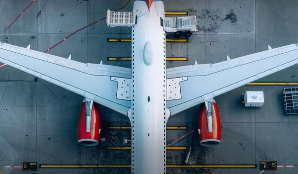 Top‑Down‑Ansicht eines Passagierflugzeugs auf dem Vorfeld eines Flughafens, mit sichtbar ausgeklappten Tragflächen und Triebwerken.