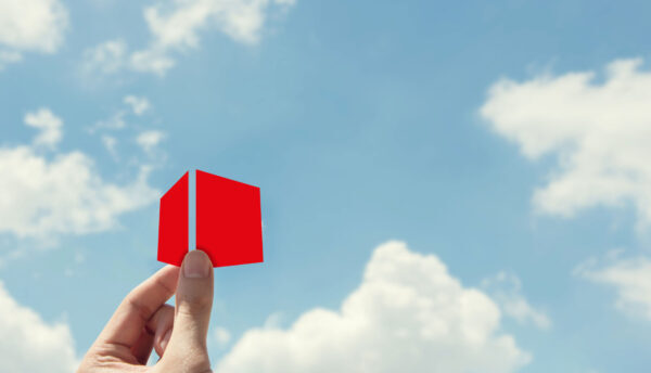 Hand hält einen kleinen roten Würfel in den Himmel, im Hintergrund blaue Sky mit weißen Wolken