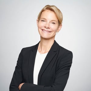 Ein professionelles Portrait von Anke Barnaschewski, die freundlich vor grauem Hintergrund in die Kamera lächelt.