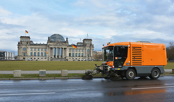 Orange Straßenreinigungsfahrzeug der BSR fährt auf nasser Straße vor dem Reichstagsgebäude in Berlin.