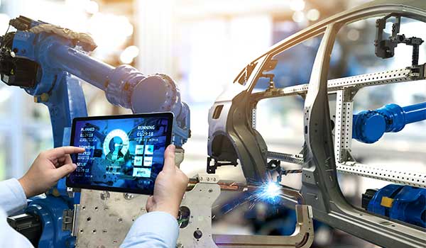 Ein Techniker überwacht mit einem Tablet die Fertigung in einer modernen Automobilproduktion, während Roboterarme an einer Karosserie arbeiten.