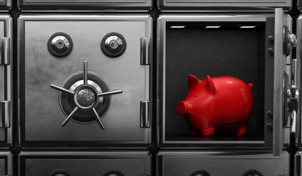 Mehrere geöffnete und geschlossene Stahlsafes in einer Wand aus Tresorfächern; eines der Fächer ist geöffnet und darin steht ein rotes Sparschwein.