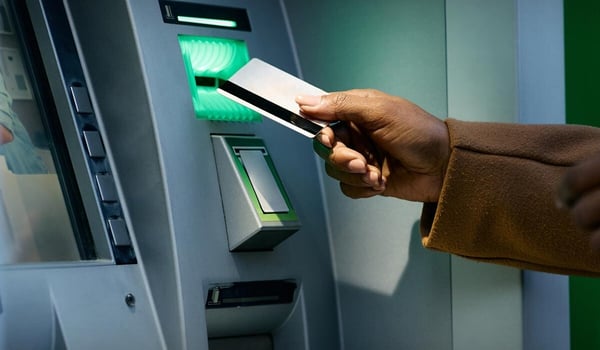 Hand führt eine Bankkarte in den Schlitz eines Geldautomaten ein; oben links steht das Logo der Sparda‑Bank.