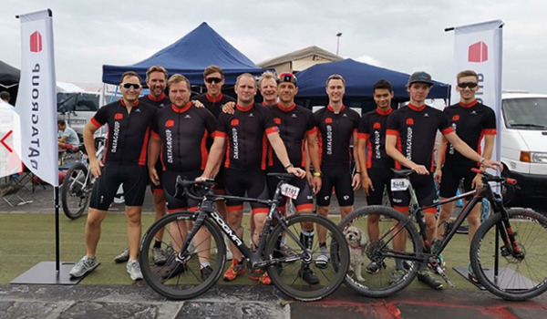 Eine Gruppe von DATAGROUP Mitarbeitenden im schwarzen und roten Endurance-Team-Outfit steht mit Rennrädern für ein Gruppenfoto zusammen.