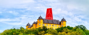 The Yellow Castle in Montabaur, with its towers and domed roof, sits on a wooded hill against a cloudy sky.