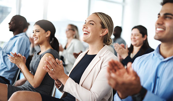 Mehrere Personen sitzen in einer Reihe und applaudieren mit fröhlichen Gesichtern während einer Veranstaltung.