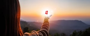 Frau steht in der Natur bei Sonnenuntergang und streckt ihre Hand nach einem leuchtenden Symbol aus das künstliche Intelligenz symbolisiert
