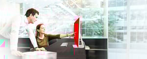Two employees working together in a modern office - a woman points at the screen, a man leans towards her with interest. Symbolic image for personal contact and direct communication at DATAGROUP.