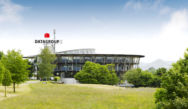 Der moderne DATAGROUP Firmensitz in Pliezhausen zeigt ein Glasgebäude mit Firmenlogo, das von grüner Landschaft umgeben ist