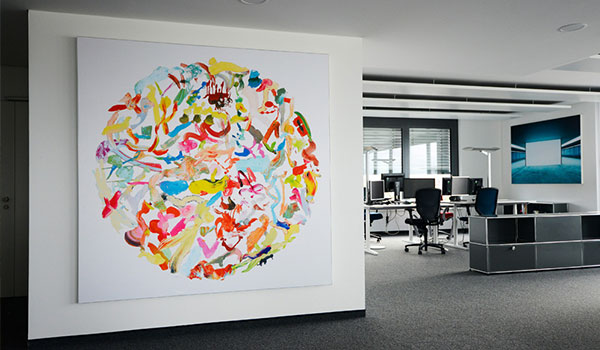 Colorful circular abstract artwork on white wall in modern office space with workstations in the background