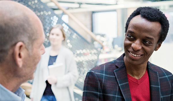 Mitarbeiterinnen und Mitarbeiter essen gemeinsam in der Kantine, einige tragen Tabletts mit Mahlzeiten, auf einem Tisch ist das rote Datagroup-Logo zu sehen.