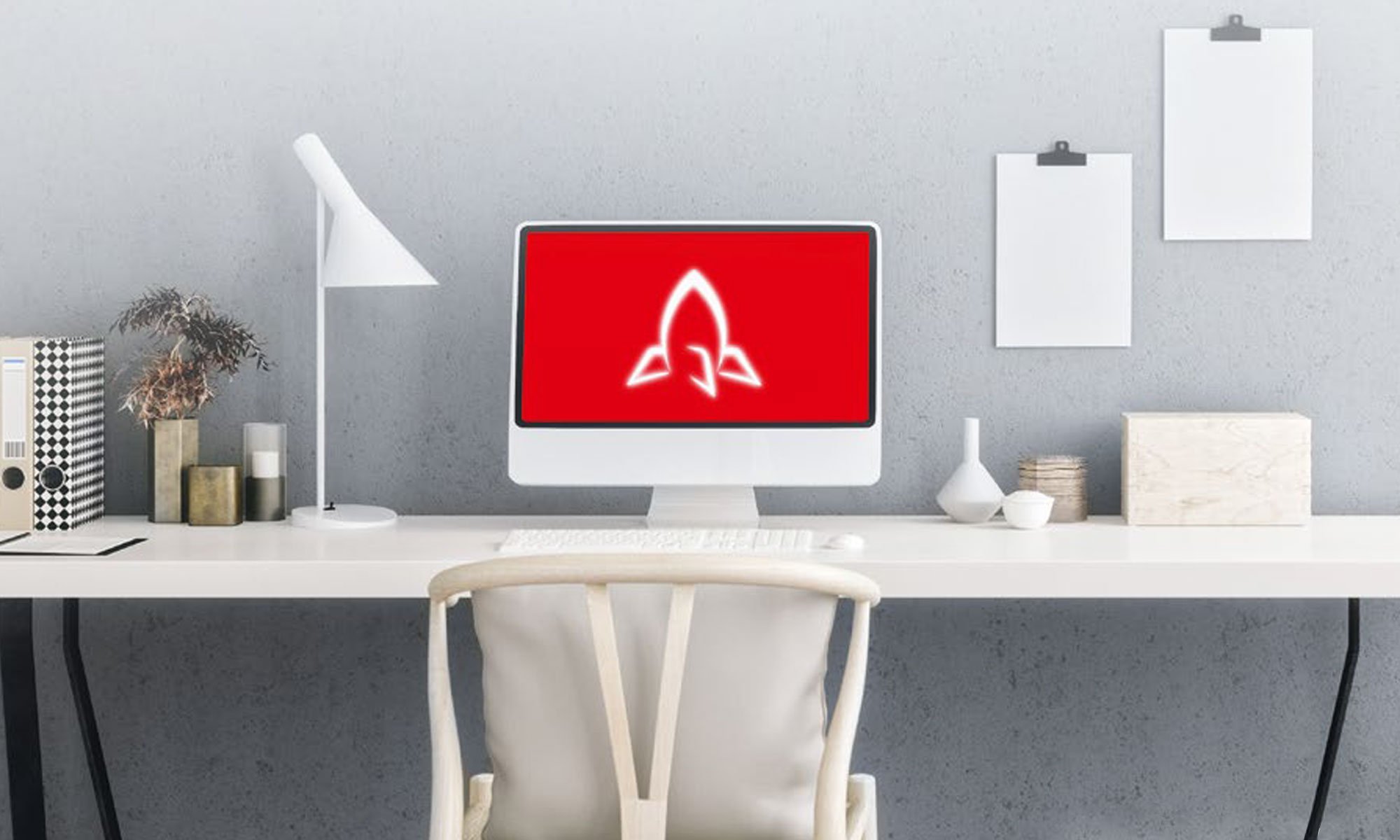 Moderner Arbeitsplatz im Homeoffice mit weißem Schreibtisch, iMac mit rotem Bildschirm und Raketen-Symbol – Symbol für den digitalen Arbeitsplatzservice von DATAGROUP mit Citrix-Lösungen