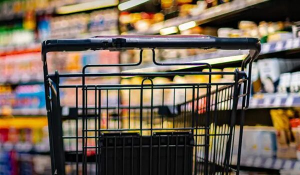 Shopping cart in a supermarket aisle, with blurred products on the shelves visible in the background.