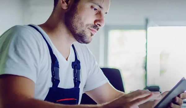 Techniker in Arbeitskleidung, der in einem hell beleuchteten, modernen Arbeitsbereich ein digitales Tablet benutzt.
