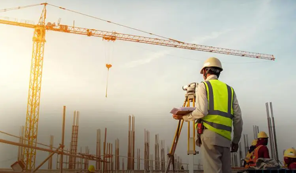 Bauarbeiter auf einer Baustelle mit Vermessungsgerät, Kran und Stahlkonstruktionen im Hintergrund bei Sonnenuntergang.