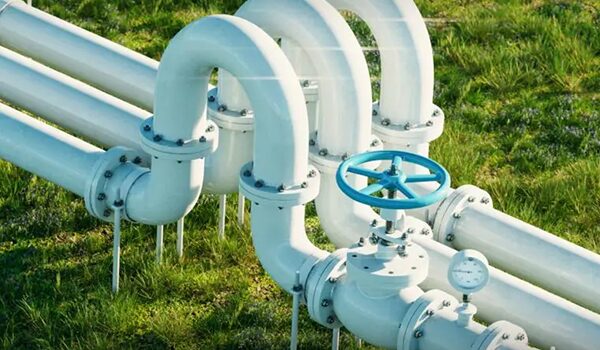 Nahaufnahme von weißen Industriepipelines mit gebogenen Verbindungsstücken und einem großen blauen Ventil, die im Freien auf einer Wiese aufgestellt sind und eine saubere Infrastruktur und ein Manometer zeigen.