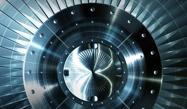 Nahaufnahme einer polierten metallischen Turbinen- oder Triebwerkskomponente mit radialen Schaufeln, die symmetrisch von einer zentralen Nabe in kühlen Blau- und Silbertönen ausgehen.