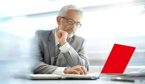 Geschäftsmann mittleren Alters arbeitet konzentriert am roten Laptop in hellem Büro mit großen Fenstern.