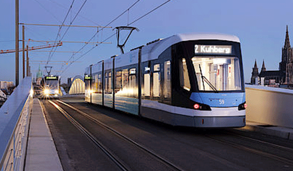 Moderne Straßenbahn der Stadtwerke Ulm fährt bei Abenddämmerung über eine Brücke.