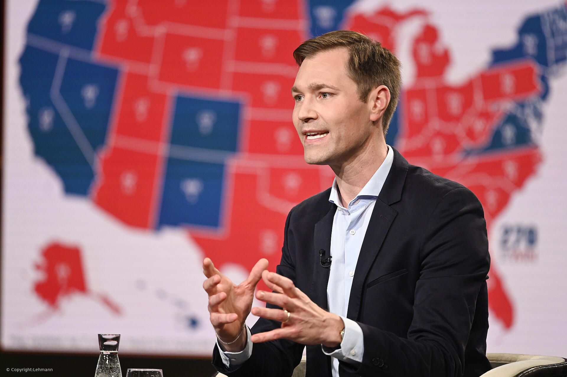 Julius van de Laar, Kampagnen- und Strategieberater, spricht beim Business Dinner Hamburg von DATAGROUP über politische Kampagnen und Kommunikation, im Hintergrund eine USA-Karte in Rot und Blau. ✅