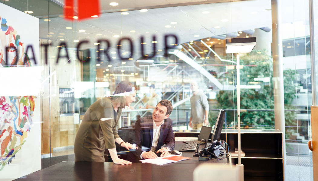 Empfangsbereich im DATAGROUP Hauptsitz Pliezhausen mit Glaswänden, Logo-Aufschrift und Mitarbeitenden im Gespräch.