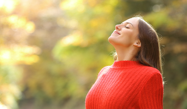 Frau im roten Pullover steht in der Natur und atmet tief durch – Symbol für bewusste Atmung und Entspannung.