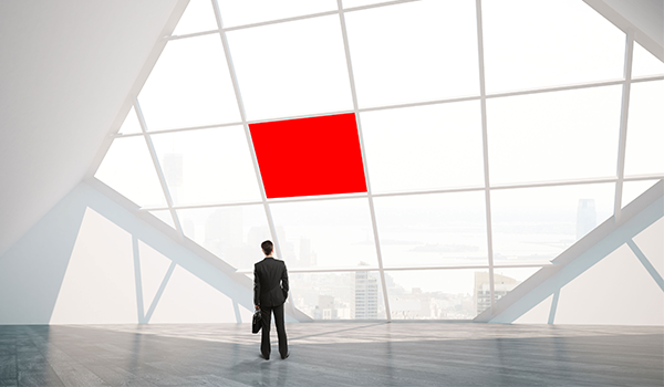 Geschäftsmann in modernem Gebäude blickt durch große Fensterfront auf eine Skyline; in der Glasfront ein rotes Quadrat als Gestaltungselement im DATAGROUP Stil.