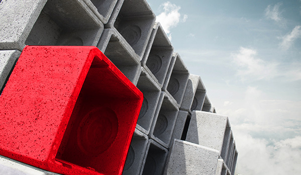 Betonwürfel gestapelt, einer in markantem Rot hervorgehoben.