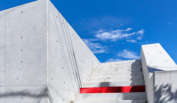 Weiße Betontreppe mit einer auffälligen roten Stufe unter blauem Himmel.