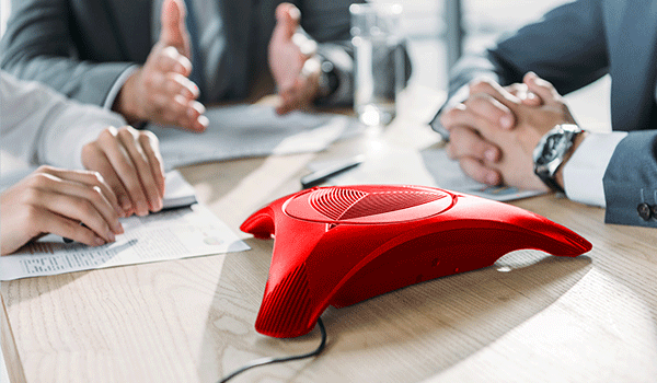 Konferenztisch mit rotem Telefonlautsprecher in der Mitte. Darstellung der Integration von Telefonie in Microsoft 365 für moderne Arbeitsplätze.