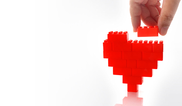 Hand setzt einen roten Baustein auf ein Herz aus Legosteinen.