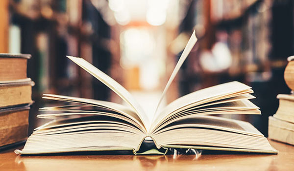 Aufgeschlagenes Buch im Vordergrund, im Hintergrund Bücherregale