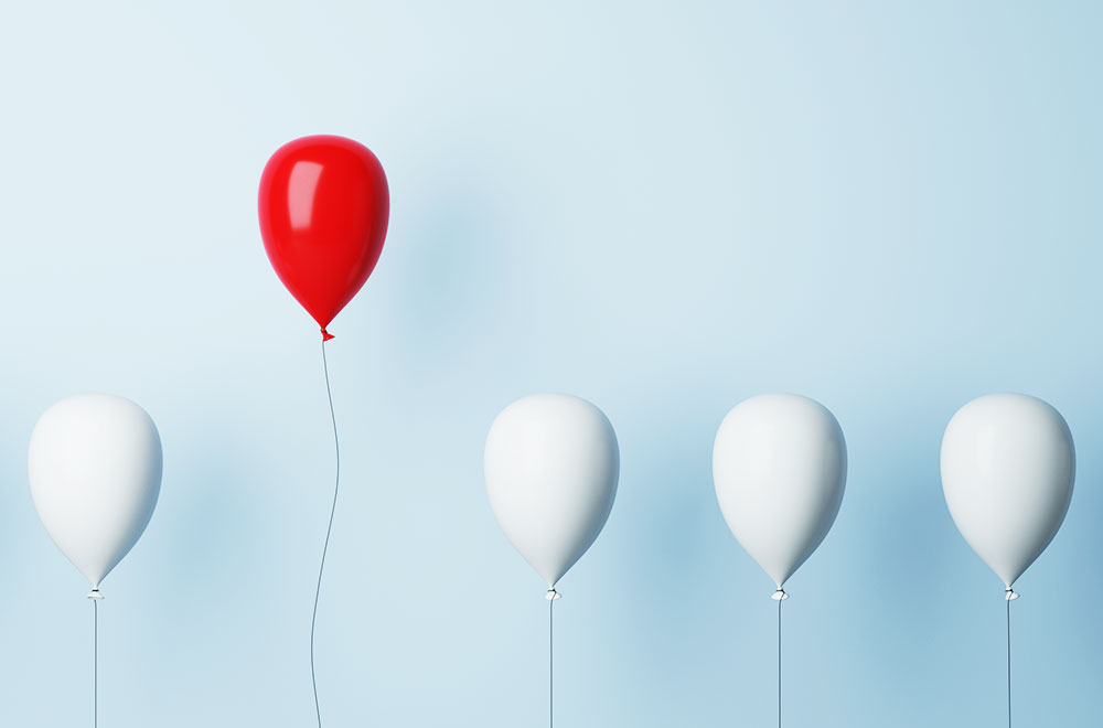 Aufsteigende weiße Luftballons, einer davon ist rot