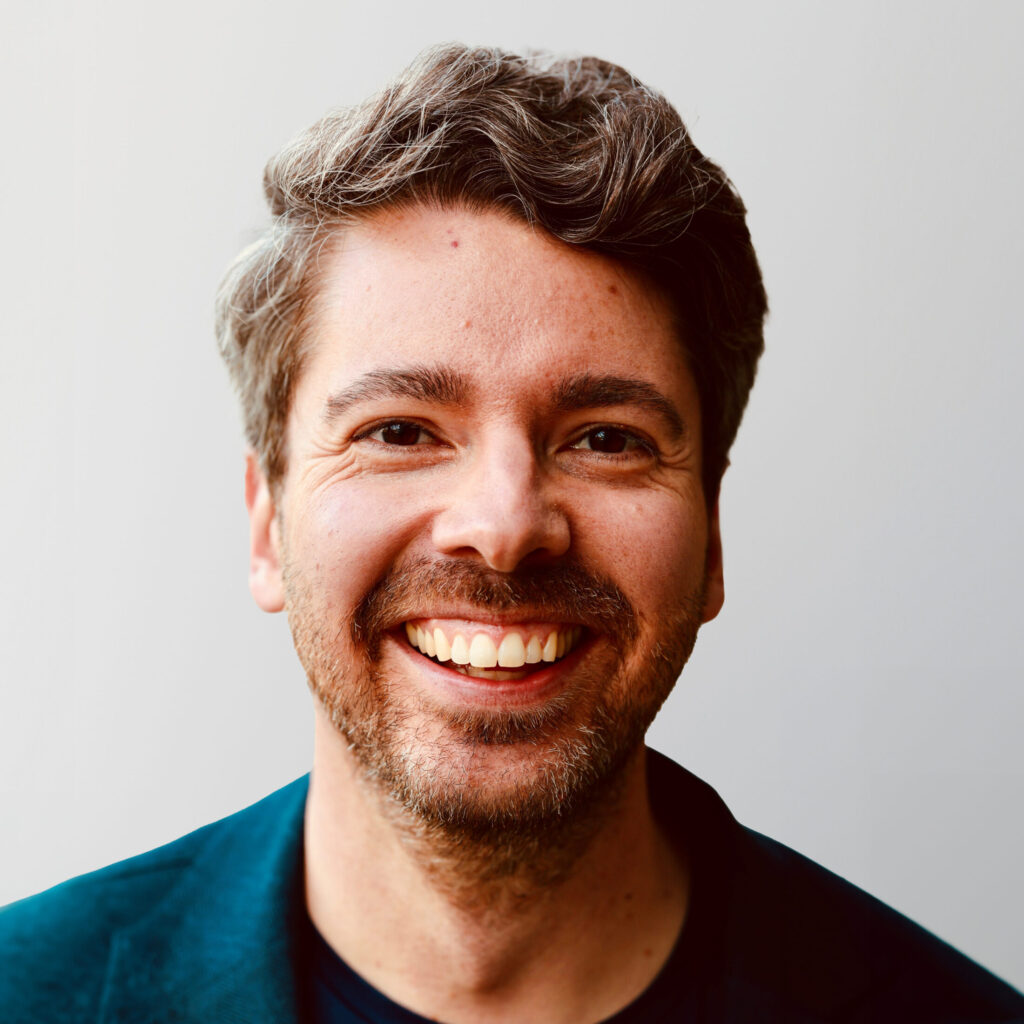 Lächelnder Mann mit grauen Haaren und Bart, der in die Kamera schaut.